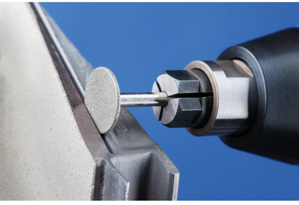 Nahaufnahme eines Rotationswerkzeugs, das Metalloberfläche mit Schleifscheibe poliert. Werkzeug in Bewegung, blaue Hintergrundfarbe.