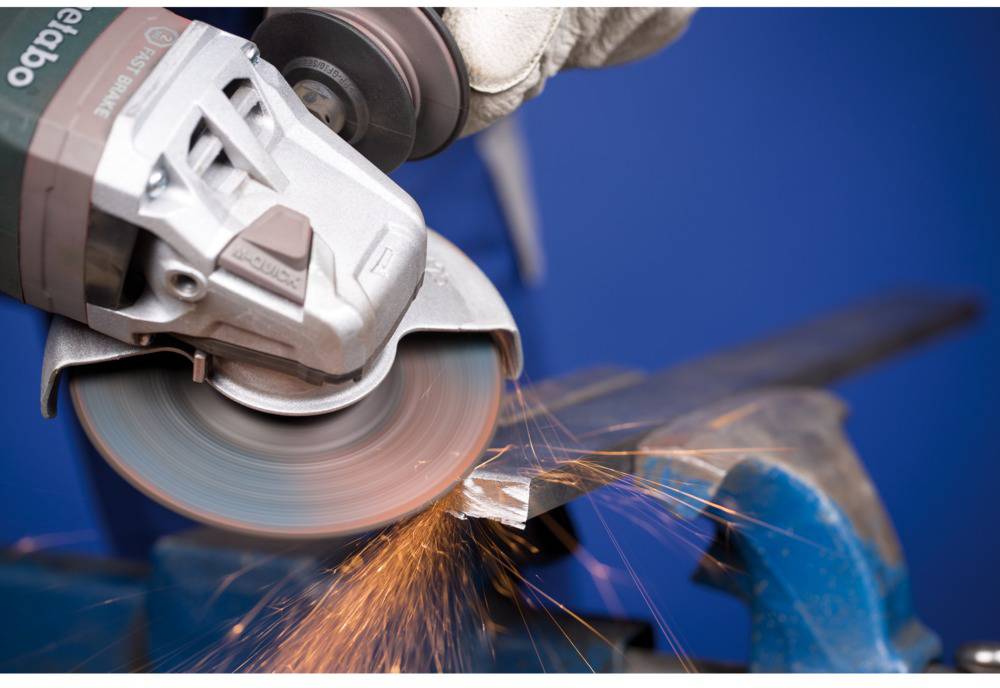 Eine Person schleift Metall mit einem Winkelschleifer, wobei Funken fliegen. Die Szene zeigt handwerkliche Arbeit in einer Werkstatt.