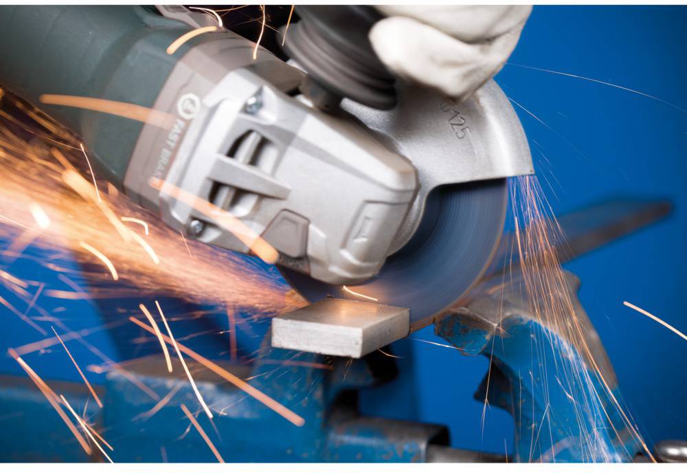 Eine Hand hält einen Winkelschleifer, der Funken sprüht, während er ein Metallstück in einem Schraubstock schneidet.