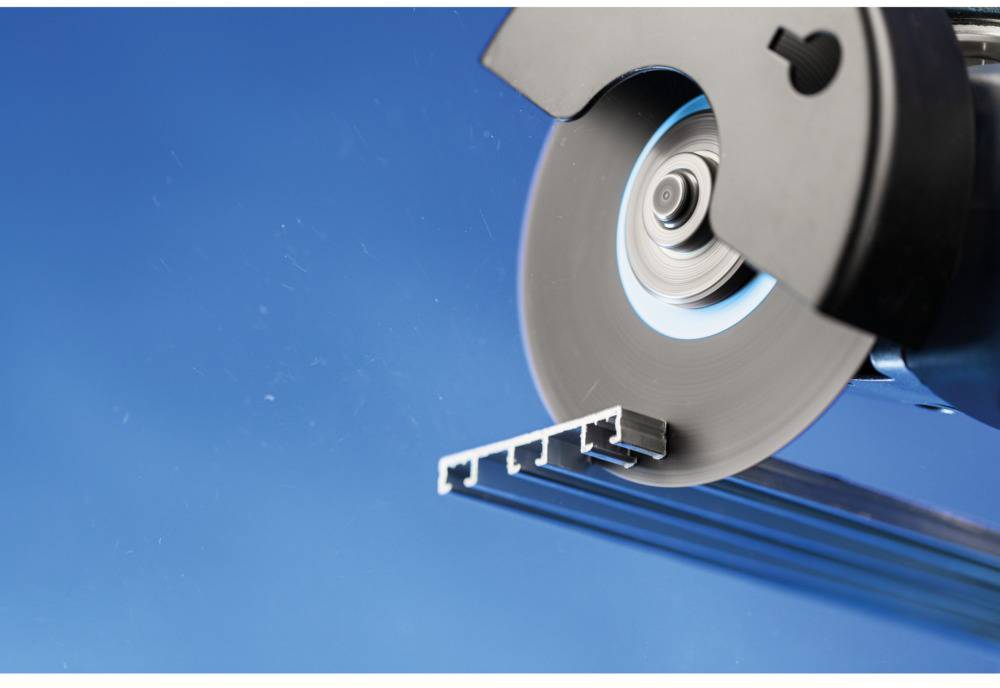 Nahaufnahme einer Metallsäge, die ein Aluminiumprofil schneidet, auf blauem Hintergrund.