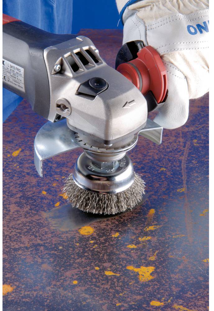 Eine Hand in Handschuh hält eine rotierende Drahtbürste, die Rost von einer Metalloberfläche entfernt.