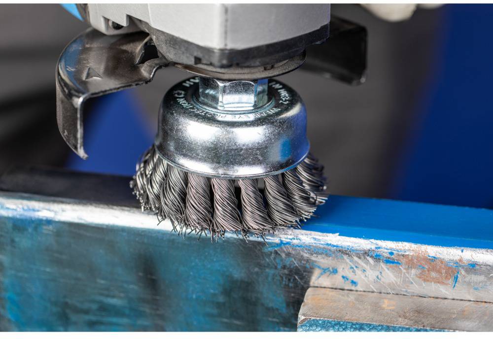 Ein rotierender Drahtbürstenaufsatz an einer Schleifmaschine reinigt eine Metalloberfläche.