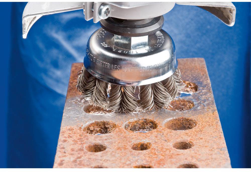 Rotierende Drahtbürste entrostet Metallfläche mit Löchern; Detailaufnahme zeigt Wirbelbewegung und Rostentfernung.