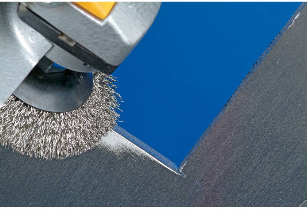 Eine Maschine mit Drahtbürste, die eine Metallkante schleift, vor einem blauen Hintergrund.