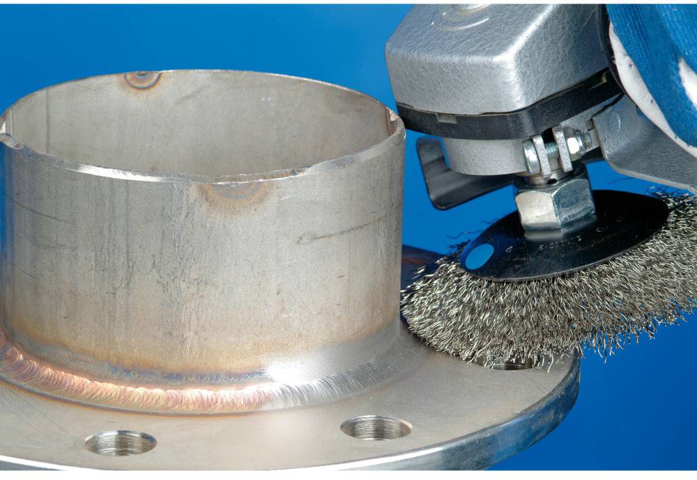 Ein Schleifgerät mit einer Drahtbürste entfernt Rost von einer Metallrohrverbindung vor einem blauen Hintergrund.