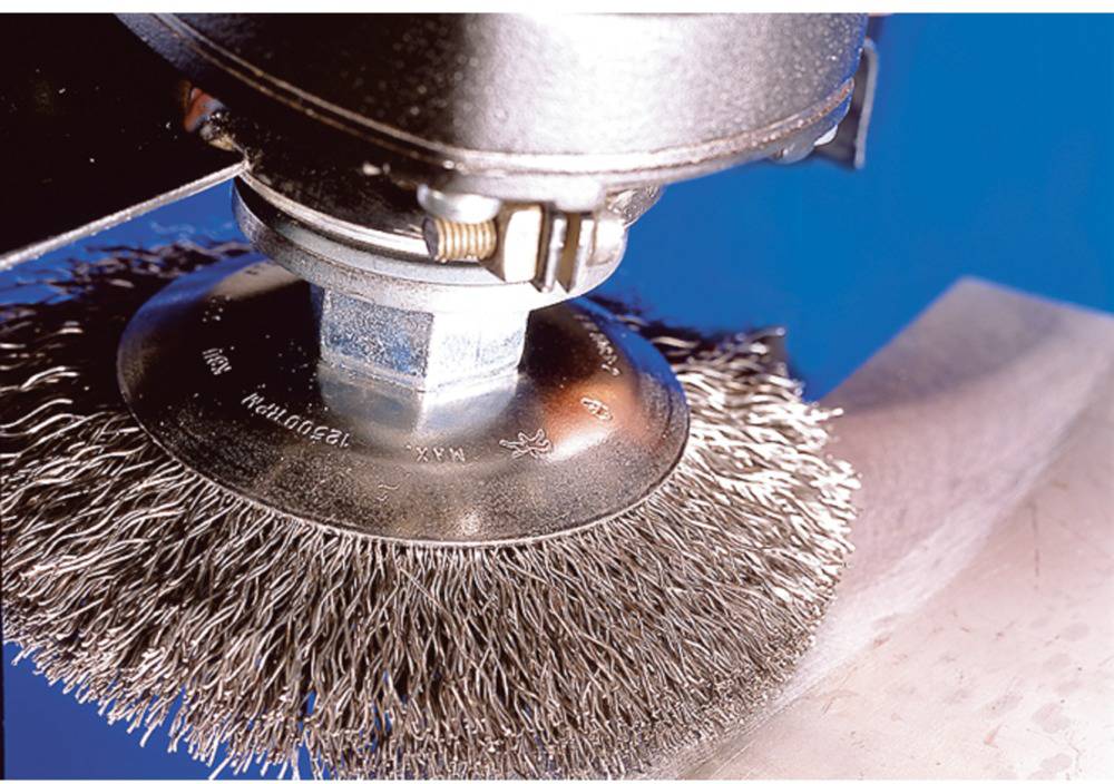 Ein rotierender Drahtbürstenaufsatz bearbeitet eine Metalloberfläche, um sie zu reinigen oder zu polieren.
