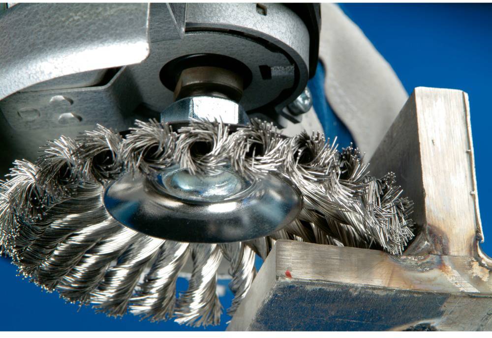 Stahlbürste, die Metalloberfläche bearbeitet. Nahaufnahme zeigt rotierende Borsten und funkenfreie Bearbeitung gegen Metallblock.