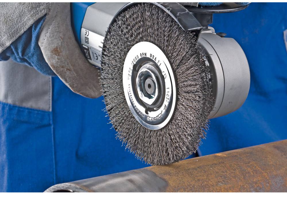 Eine Person schleift mit einer Drahtbürste den Rost von einem Metallrohr ab.