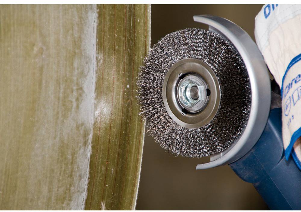 Eine Maschine mit Drahtbürste bearbeitet die metallische Oberfläche eines Werkstücks. Die Bürste entfernt Material vom Rand.