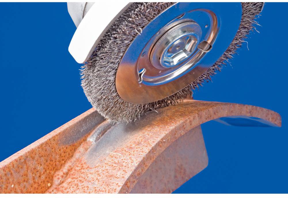 Drahtbürste, die Korrosion von einem gekrümmten Metallstück entfernt. Intensiver blauer Hintergrund.