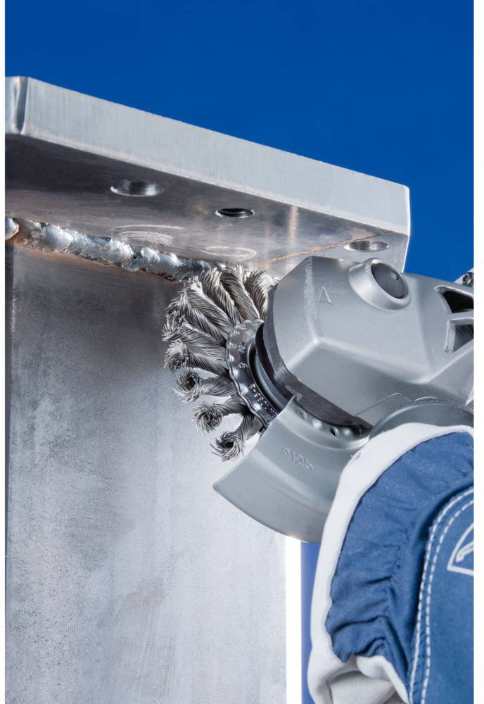 Ein Roboterarm mit Drahtbürstenaufsatz reinigt Schweißnähte auf einer Metalloberfläche gegen blauen Hintergrund.