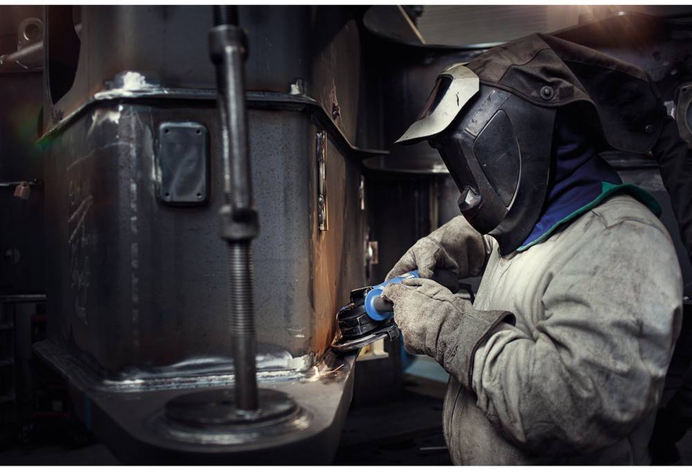 Eine Person trägt Schutzkleidung und schweißt Metall in einer Werkstattumgebung.