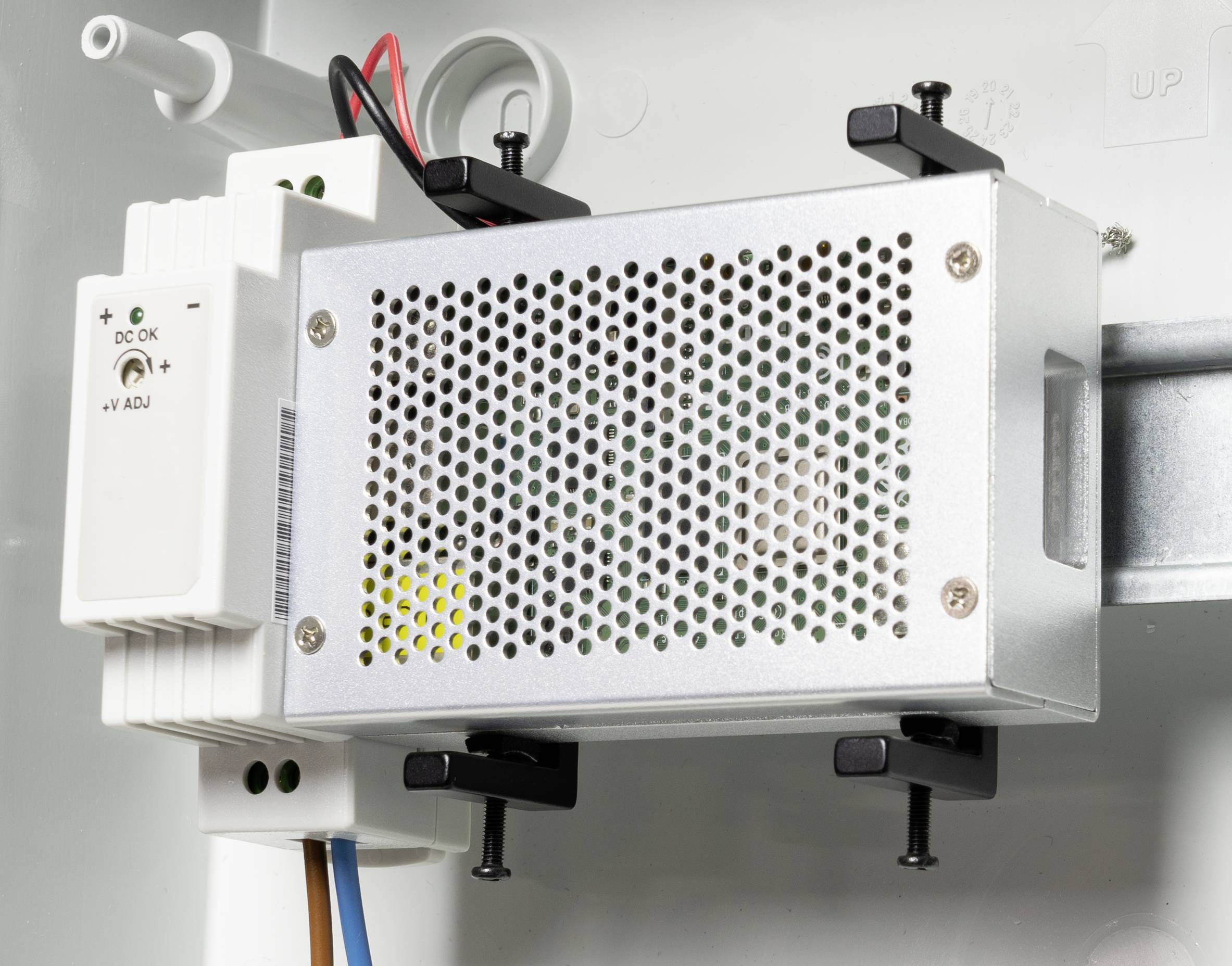 Metallene, perforierte Abdeckung einer elektrischen Komponente, befestigt mit Schrauben. Daneben ein kleines weißes Modul mit einer grünen LED.