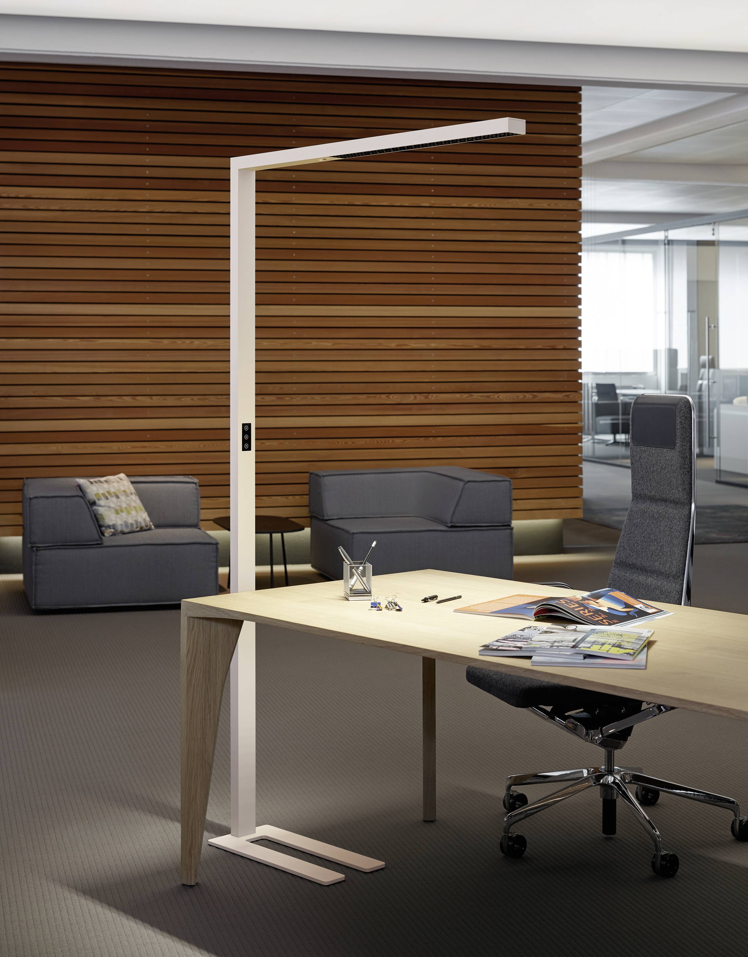 Ein modernes Büro mit einem Schreibtisch aus Holz und einer Stehleuchte. Ein gepolsterter Stuhl und ein Sofa stehen im Hintergrund.