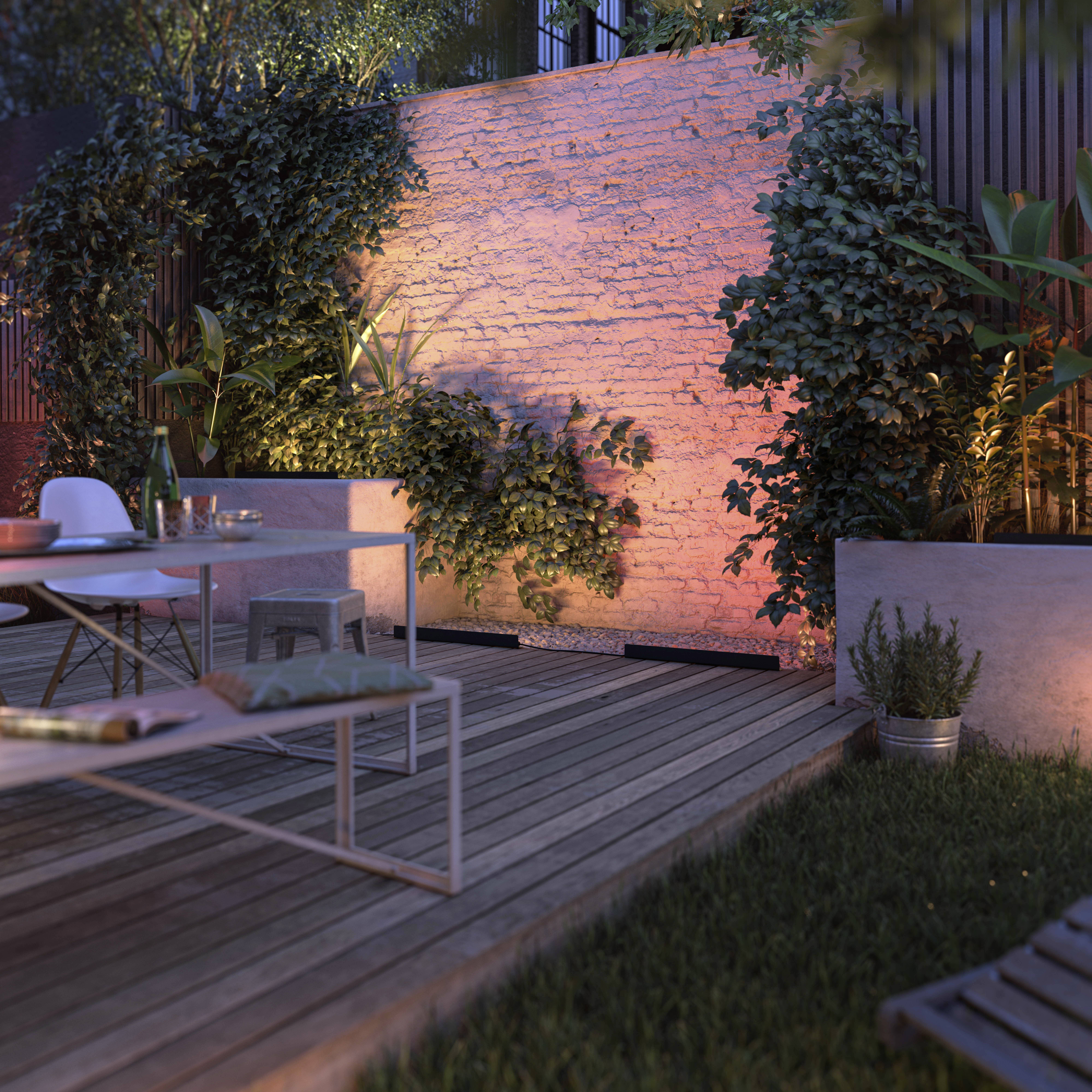 Gemütliche Terrasse bei Dämmerung mit Holzboden, Tisch mit Stühlen, Pflanzenwand und stimmungsvoller Beleuchtung.