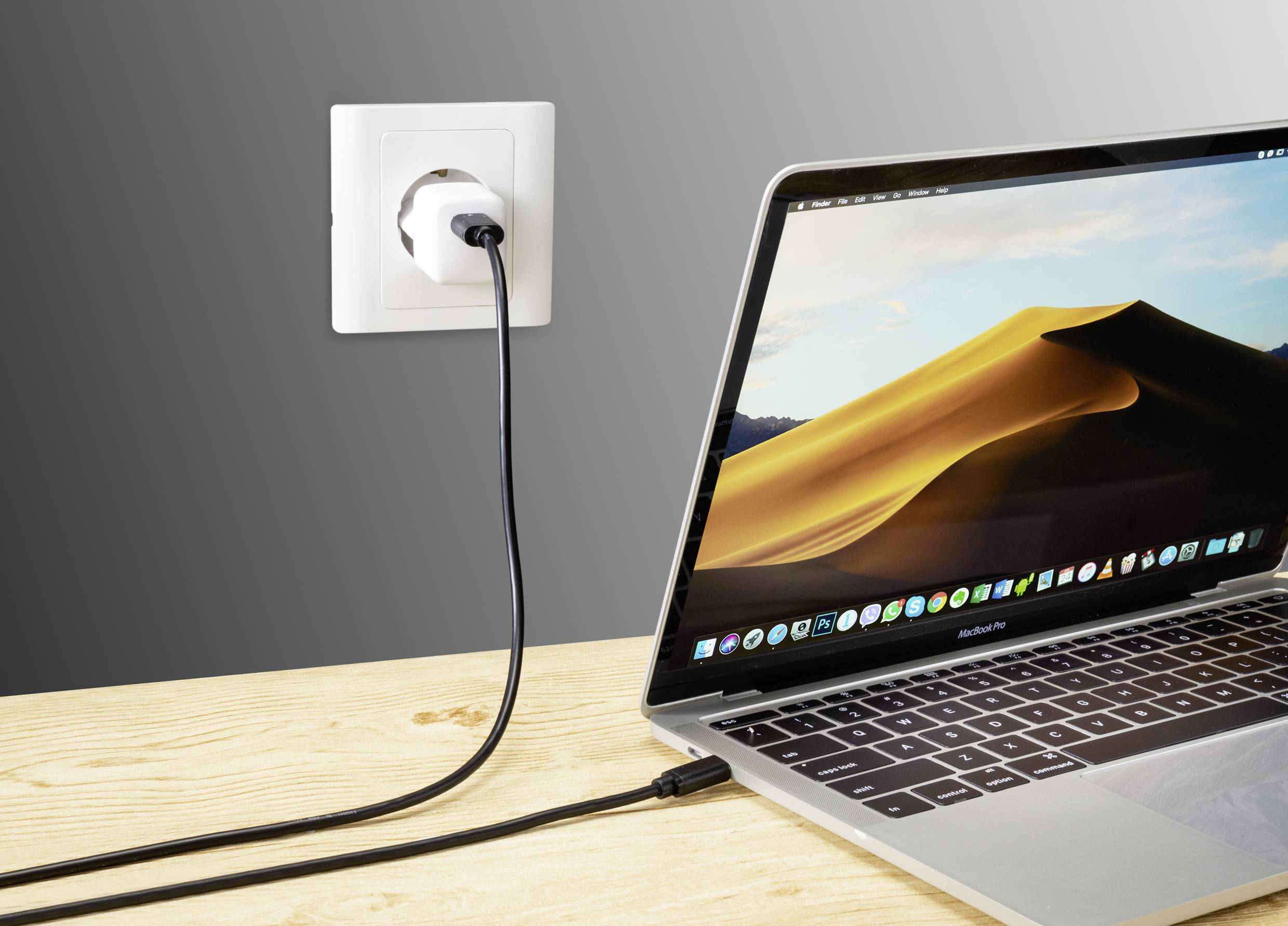 Ein Laptop ist mit einem Ladekabel an eine Steckdose angeschlossen. Der Bildschirm zeigt eine Wüstenlandschaft.