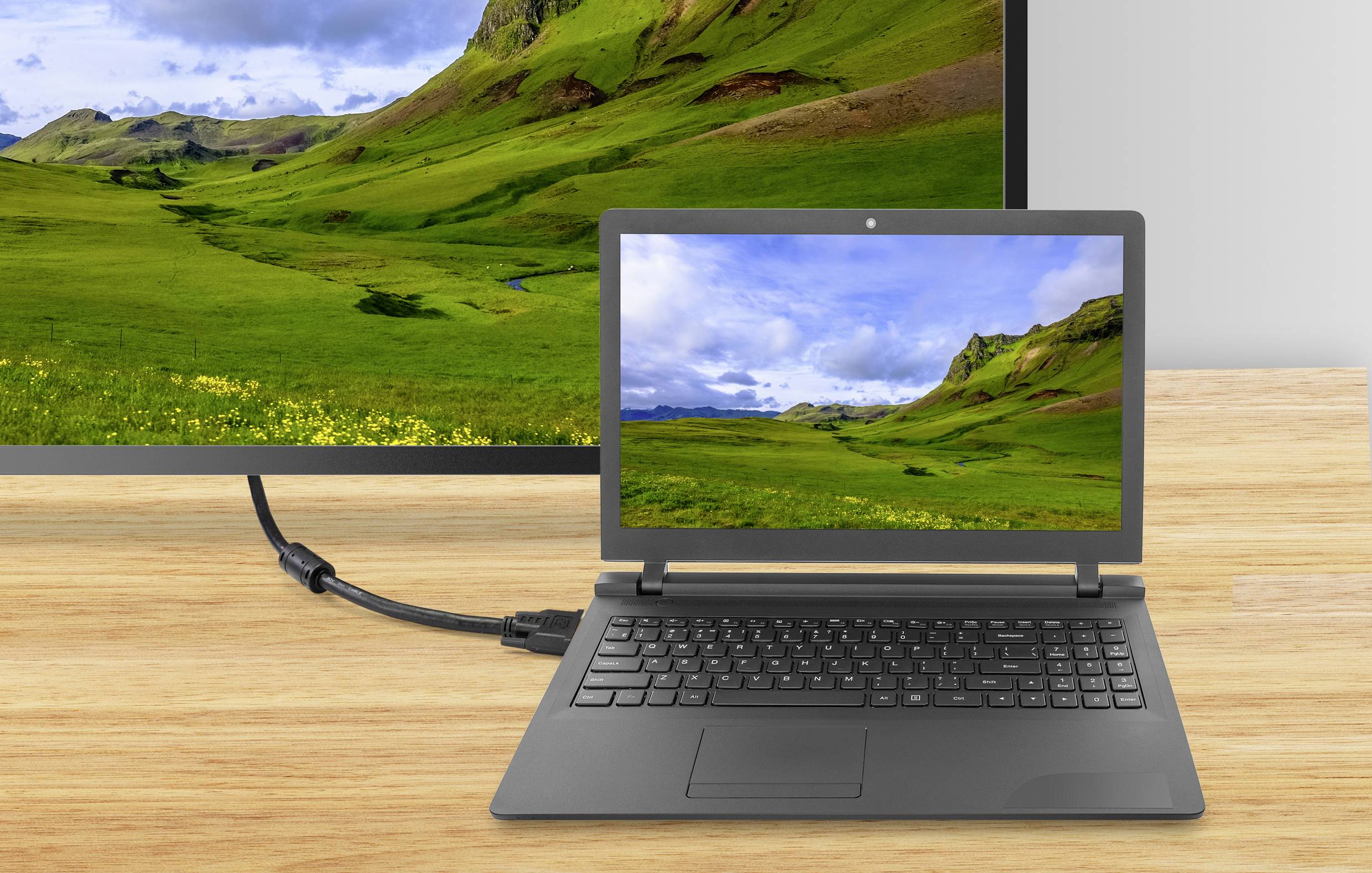 Ein Laptop, der mit einem HDMI-Kabel an einen größeren Monitor angeschlossen ist, beide zeigen ein Bild von grünen Hügeln und Wolken.
