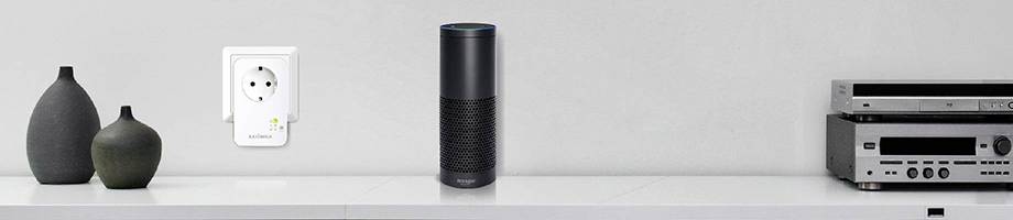 Ein smarter Lautsprecher auf einem Regal neben modernen Vasen, einer Steckdose und einem Hi-Fi-System.