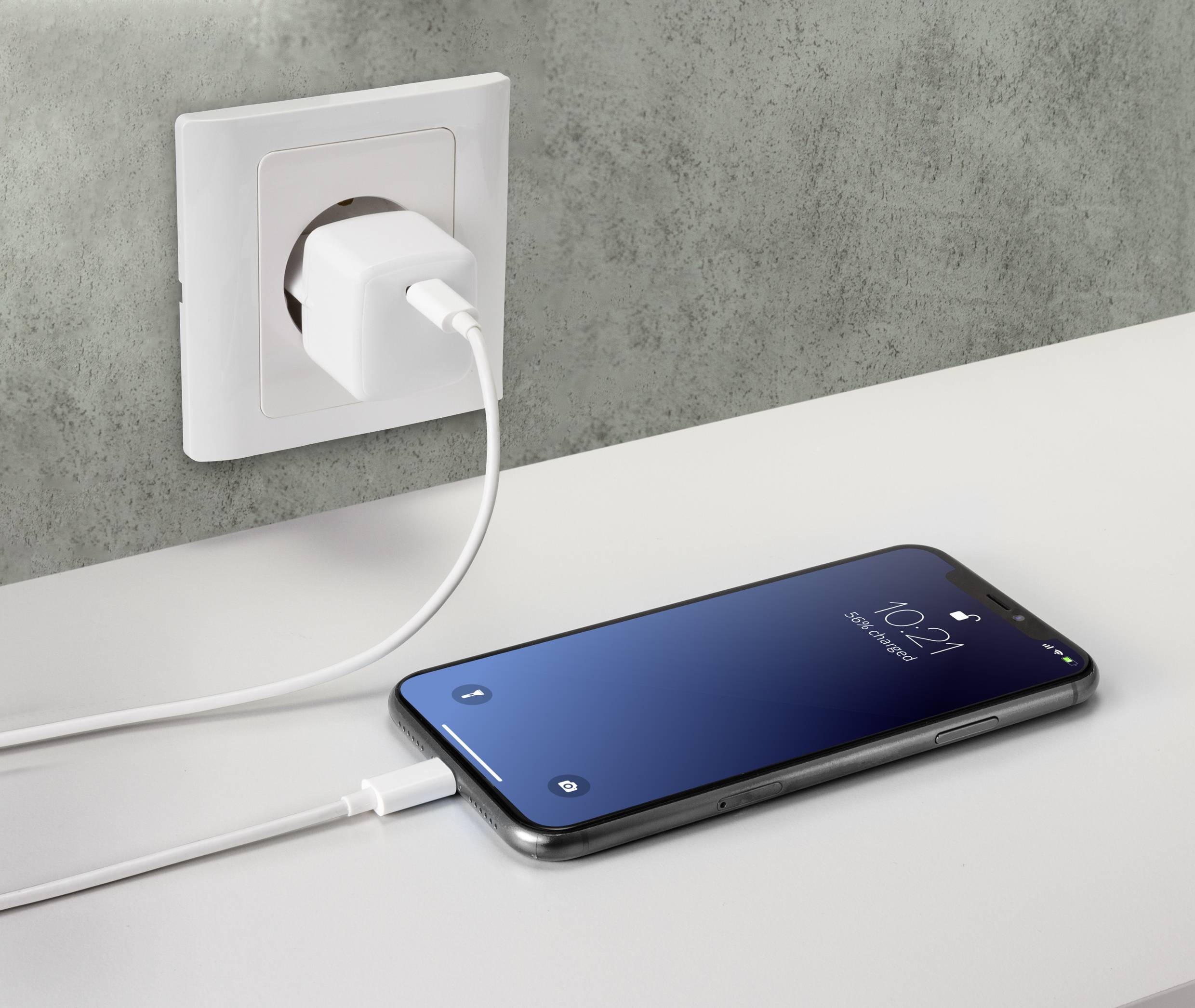 Ein Smartphone liegt auf einem Tisch und ist über ein Netzkabel mit einer Steckdose verbunden. Das Display zeigt die Uhrzeit 10:21.