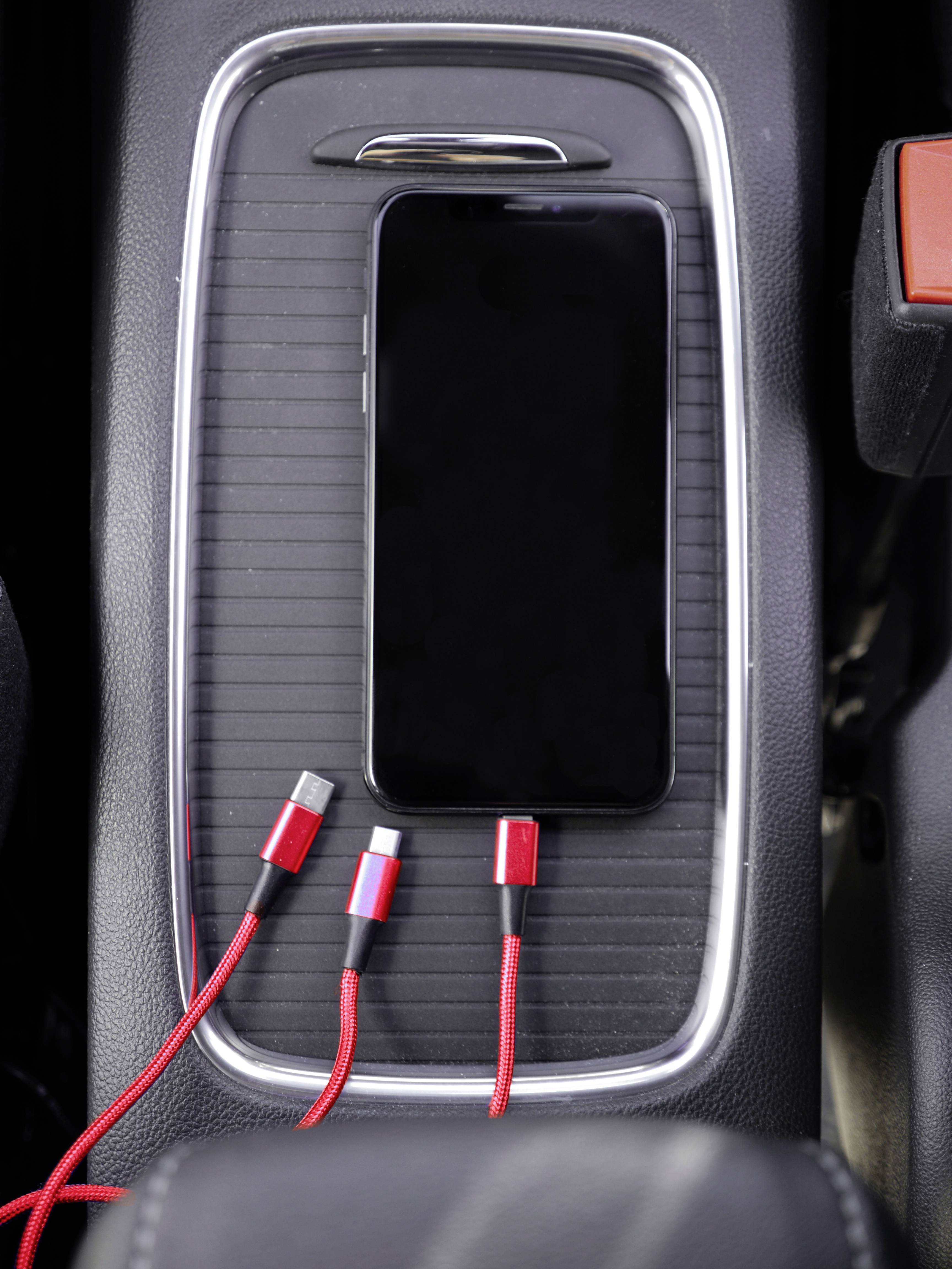 Smartphone liegt in Autoablage mit angeschlossenen roten Ladekabeln.
