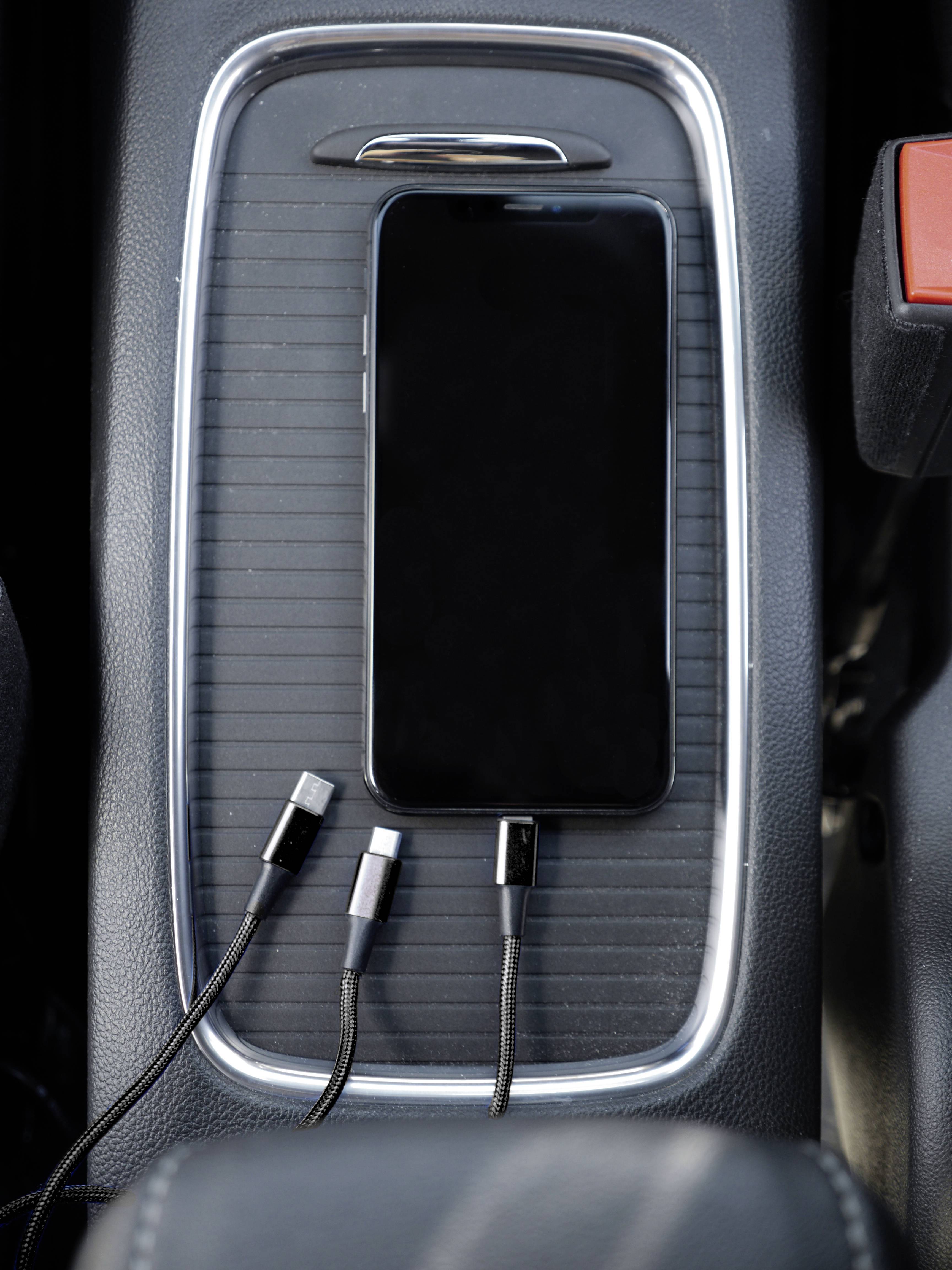 Ein Smartphone liegt auf einer Mittelkonsole im Auto neben drei verschiedenen Ladekabeln.