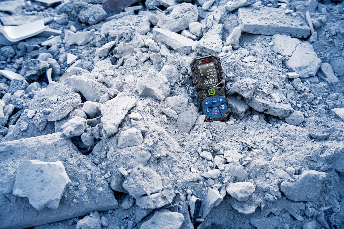 Ein Mobiltelefon liegt auf Trümmern, umgeben von Schutt und Betonbrocken, in einer Umgebung, die auf eine Katastrophe hindeutet.