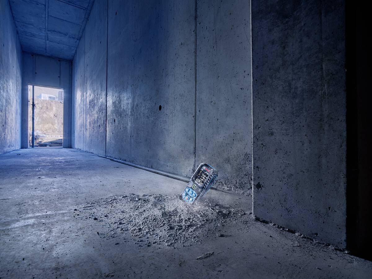 Eine Wasserflasche steckt in einem Betonboden eines leeren, grauen Flurs und erzeugt eine Delle im Boden. Im Hintergrund ist ein offener Ausgang.