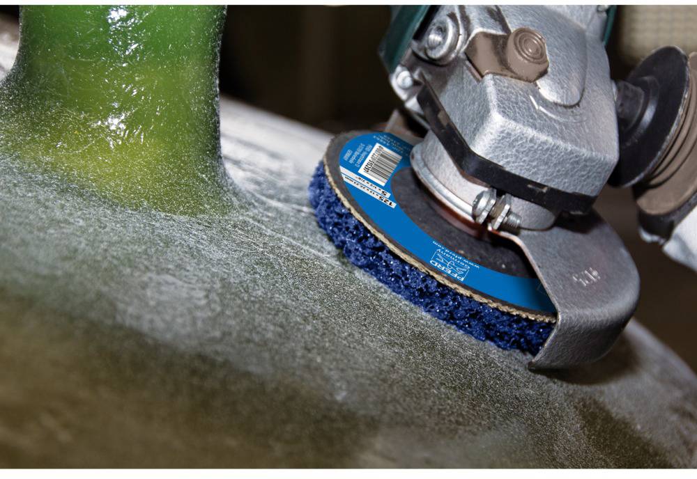 Ein Winkelschleifer bearbeitet eine Glasfaseroberfläche, Abrasionswerkzeug mit blauem Schleifpad gleitet über das Material.
