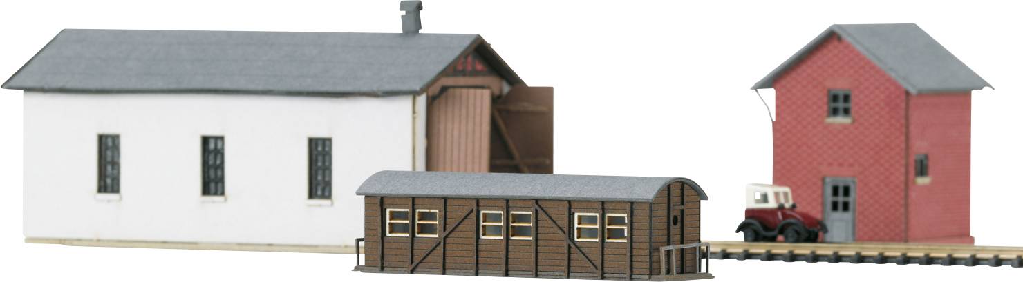 Drei Modellgebäude: ein weißes Gebäude, ein braunes Lagerhaus und ein rotes Gebäude. Ein kleiner Lastwagen steht daneben.