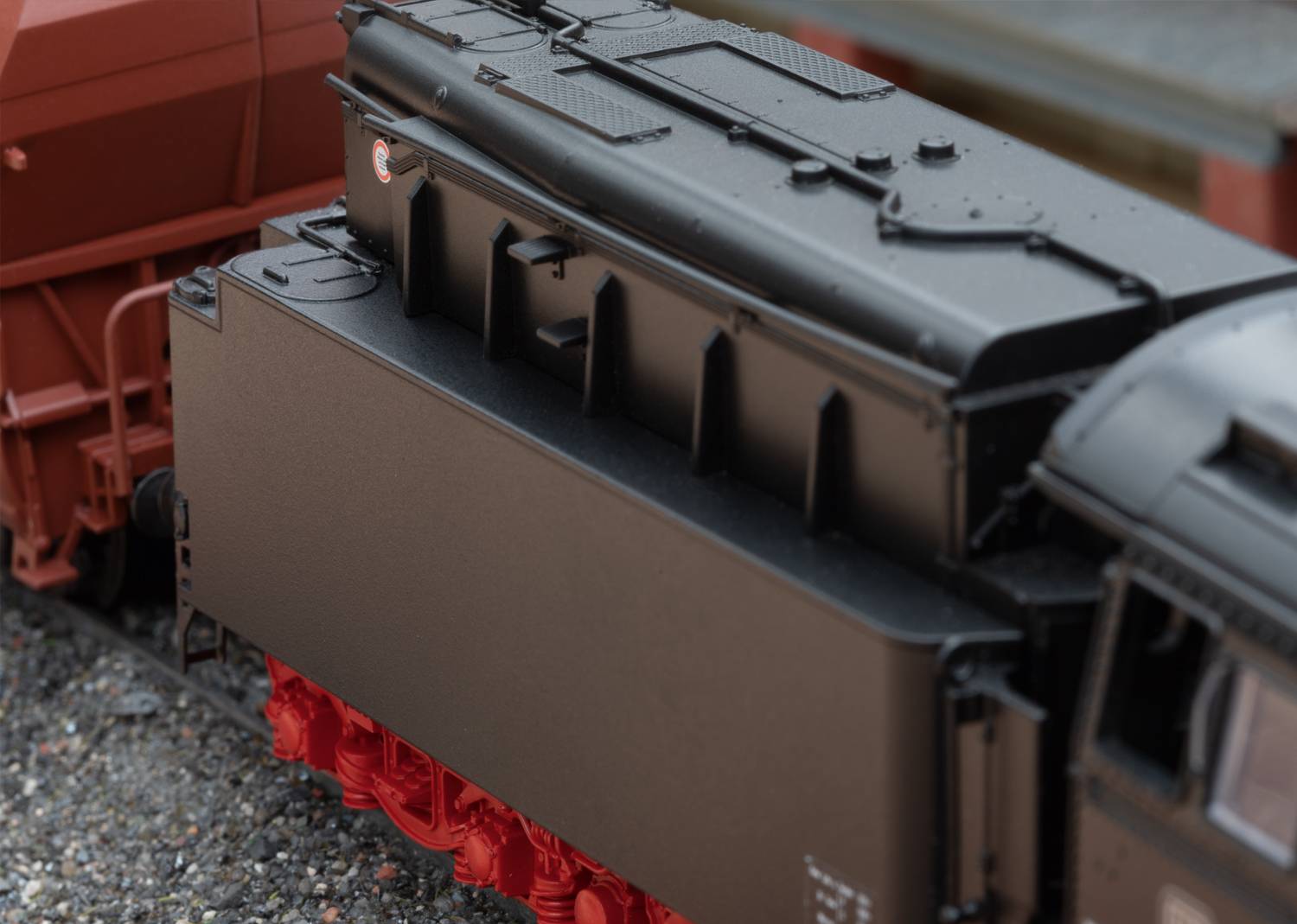 Ein Modell einer Dampflokomotive in schwarz-roter Farbgebung, seitliche Ansicht. Sie ist neben einem Güterwagen aufgestellt.