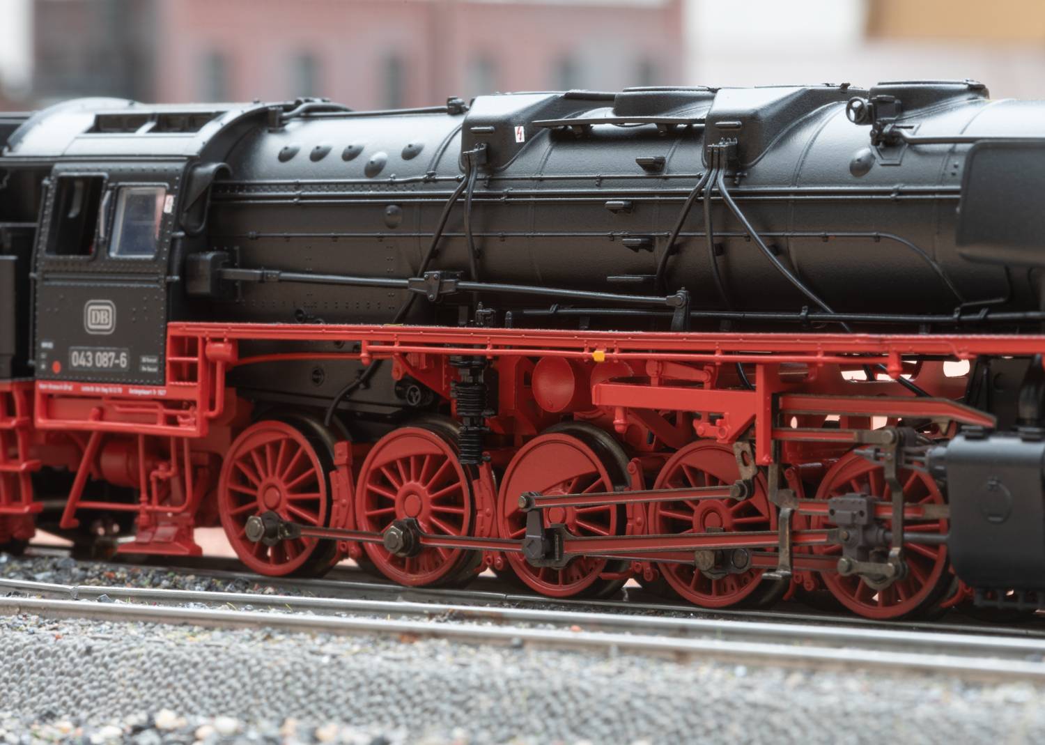 Schwarze Dampflokomotive mit roten Rädern auf einem Gleis. Die Lokomotive hat sichtbare Details wie Rohre und Bolzen. Im Hintergrund unscharf.