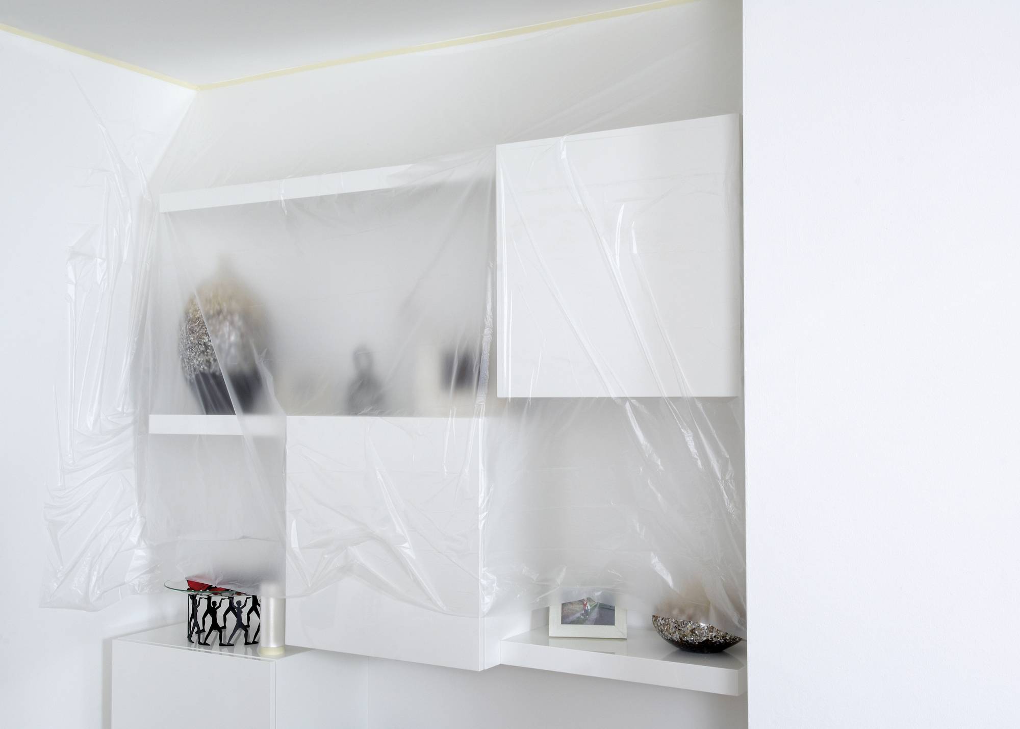 Bild eines teilsanierten Zimmers. Einbauschrank ist mit Plastikfolie abgedeckt, um Staub zu vermeiden. Regal zeigt Bücher und Deko.