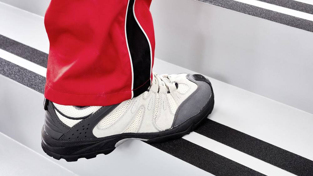 Person mit roten Hosen steigt eine Treppe hinauf. Fokus auf weißen Sportschuh.