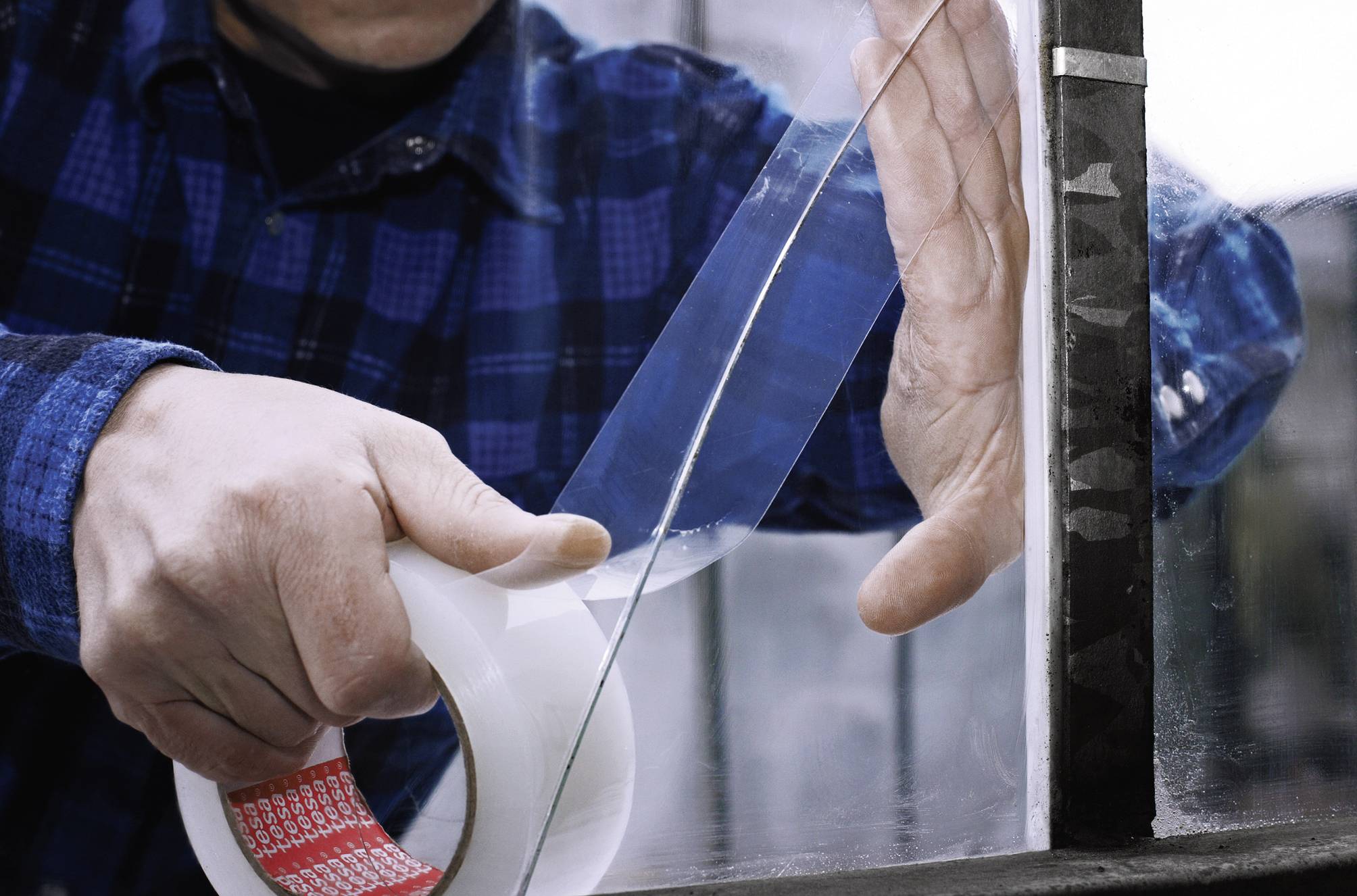 Eine Person befestigt durchsichtiges Klebeband an einer Fensterscheibe, möglicherweise für Reparatur- oder Isolationszwecke.