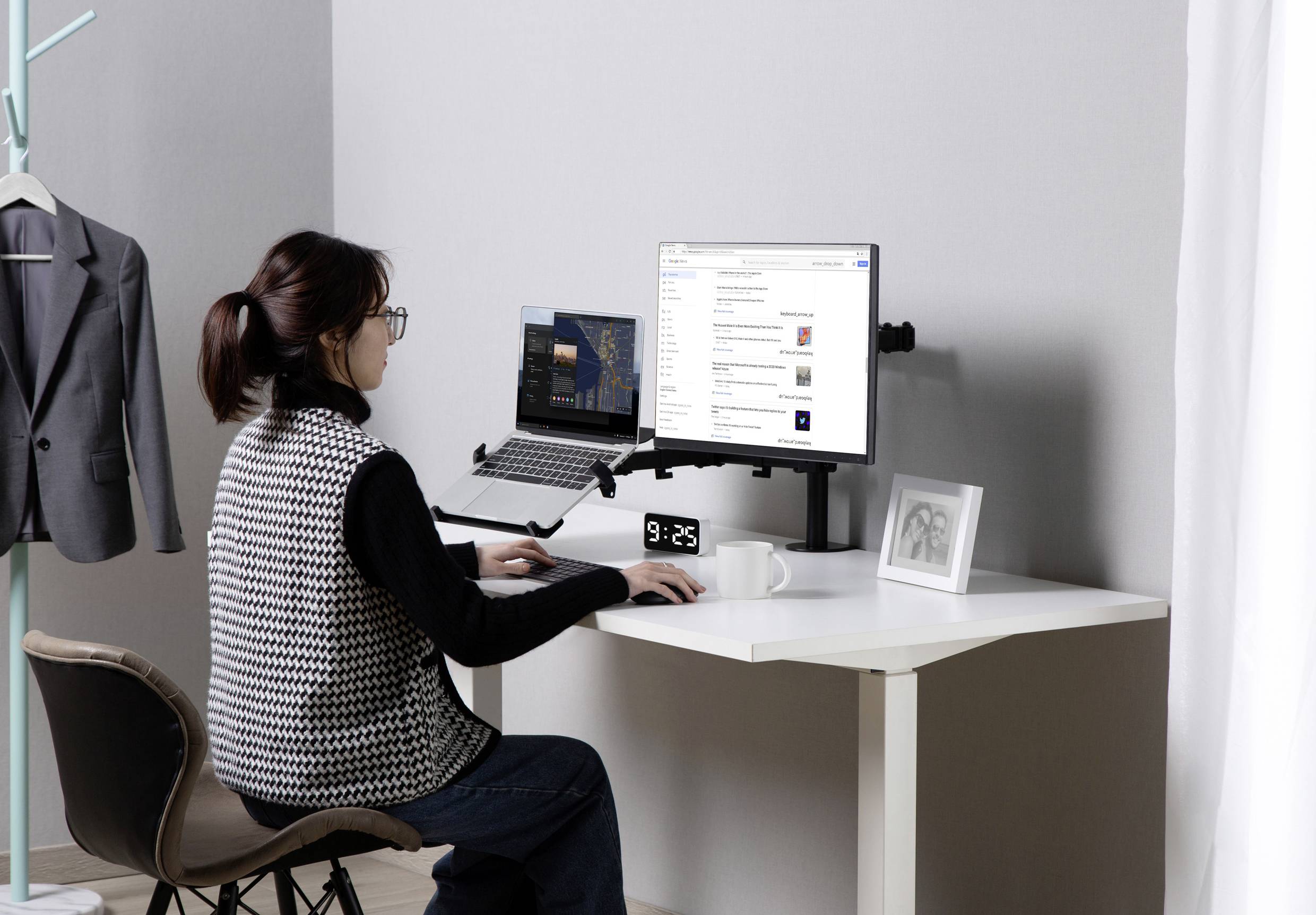 Frau arbeitet an einem Schreibtisch mit Laptop und Monitor. Die Umgebung ist modern und ordentlich, mit einem hängenden Blazer im Hintergrund.