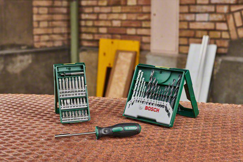 Bohrer- und Schraubendreher-Sets von Bosch auf einem Tisch, Hintergrund mit Ziegelwand und Baumaterialien.