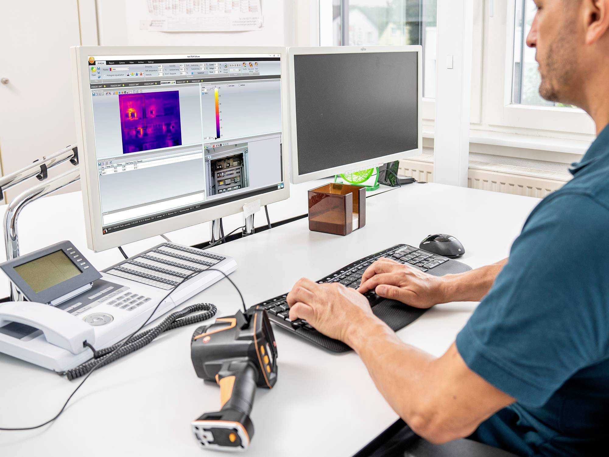 Ein Mann sitzt an einem Schreibtisch und analysiert Wärmebilddaten auf einem Computerbildschirm. Neben ihm liegt ein Infrarotkamera-Gerät.