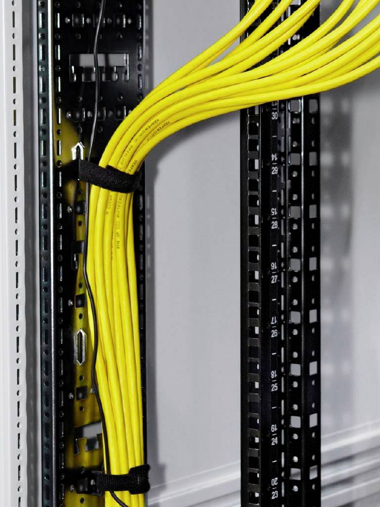 Gelbe Netzwerkkabel sind in einem Server-Rack organisiert und verlaufen vertikal an der schwarzen Struktur entlang.