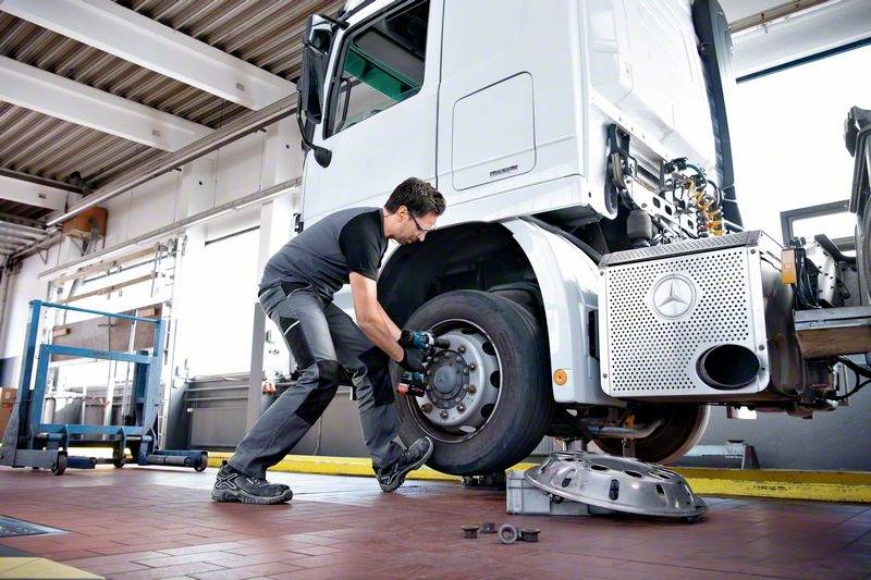 Ein Mechaniker wechselt in einer Werkstatt das Rad eines Lkw. Der Lkw ist aufgebockt. Neben ihm liegen Werkzeuge und eine Radkappe.