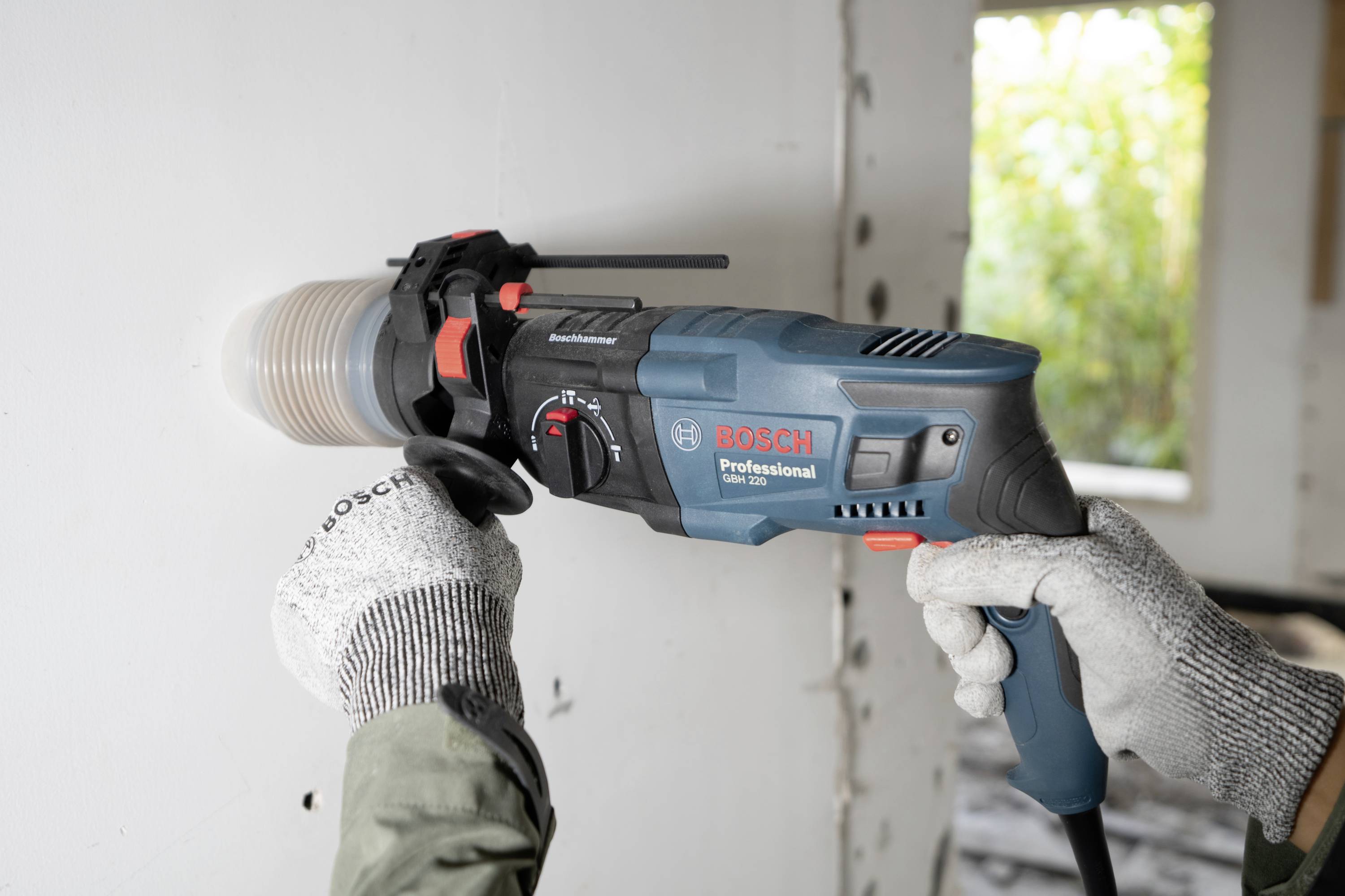 Person verwendet einen Bosch-Profibohrer, um in einer weißen Wand ein rundes Loch zu bohren. Hintergrund zeigt Baustelle.