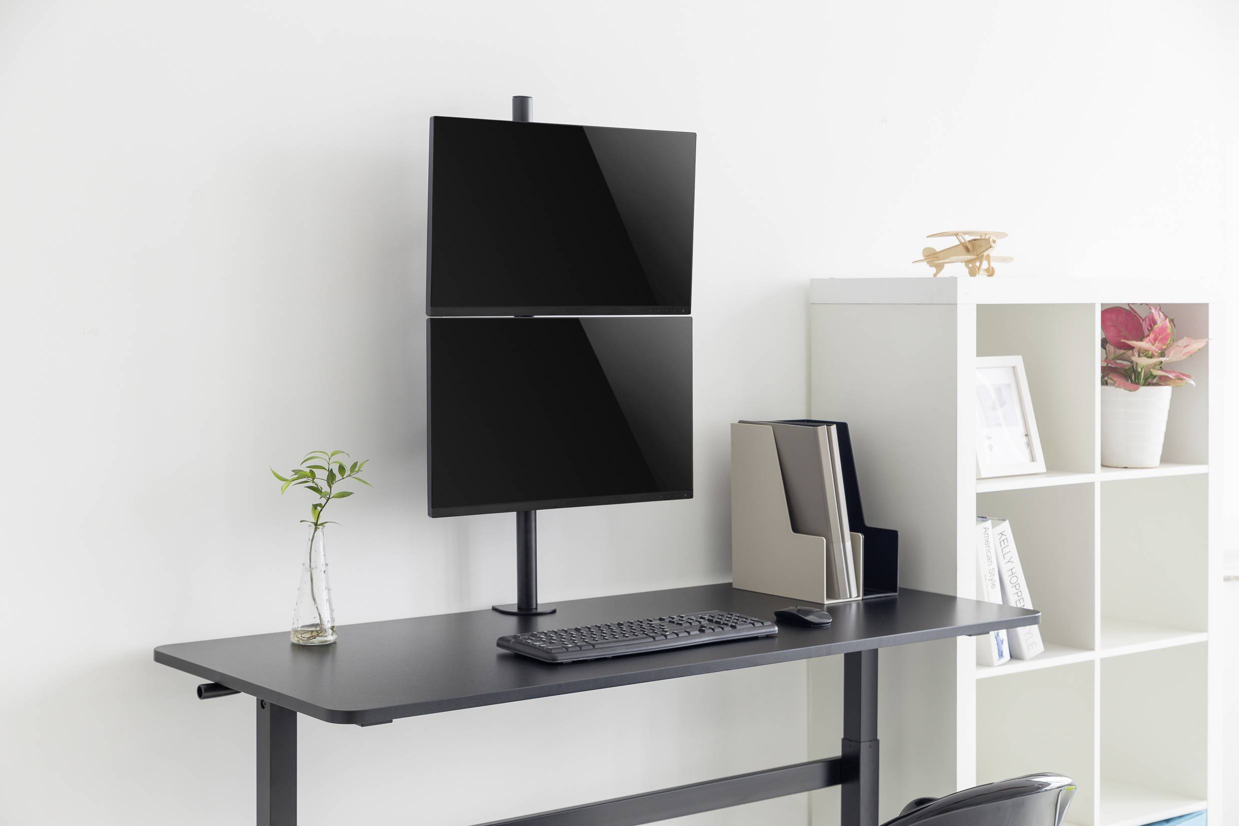 Ein eleganter Stehschreibtisch mit zwei vertikalen Monitoren, Tastatur, Maus und einem kleinen Pflanzentopf daneben vor einem hellen Hintergrund.