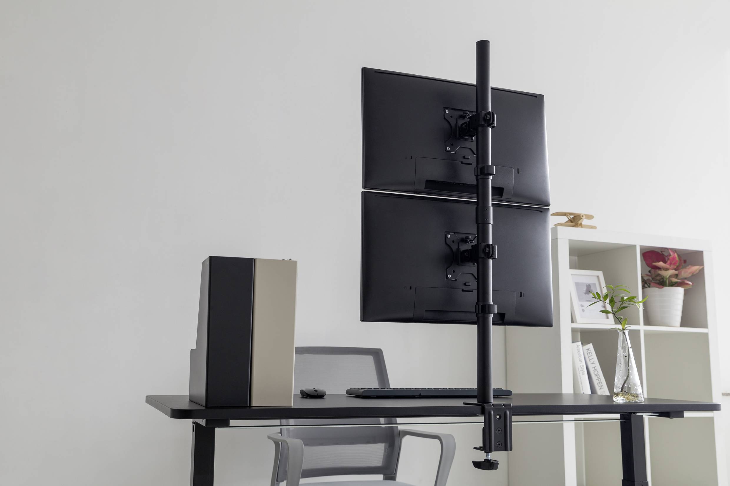 Ein moderner Arbeitsplatz mit einem schwarzen Schreibtisch, einem grauen Bürostuhl und zwei übereinander montierten Bildschirmen.