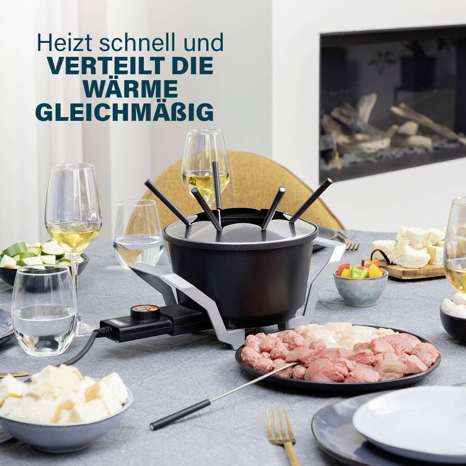Ein Tisch mit einem Fondue-Set im Mittelpunkt, umgeben von geschnittenem Gemüse, Brot, Fleisch und Weingläsern. Links oben steht: 'Heizt schnell und verteilt die Wärme gleichmäßig'.