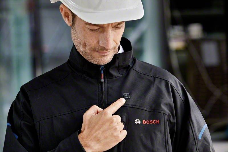 Arbeitskraft in Schutzhelm zeigt auf ein elektronisches Modul an einer Jacke mit 'BOSCH'-Logo. Kontext: Produktvorstellung.