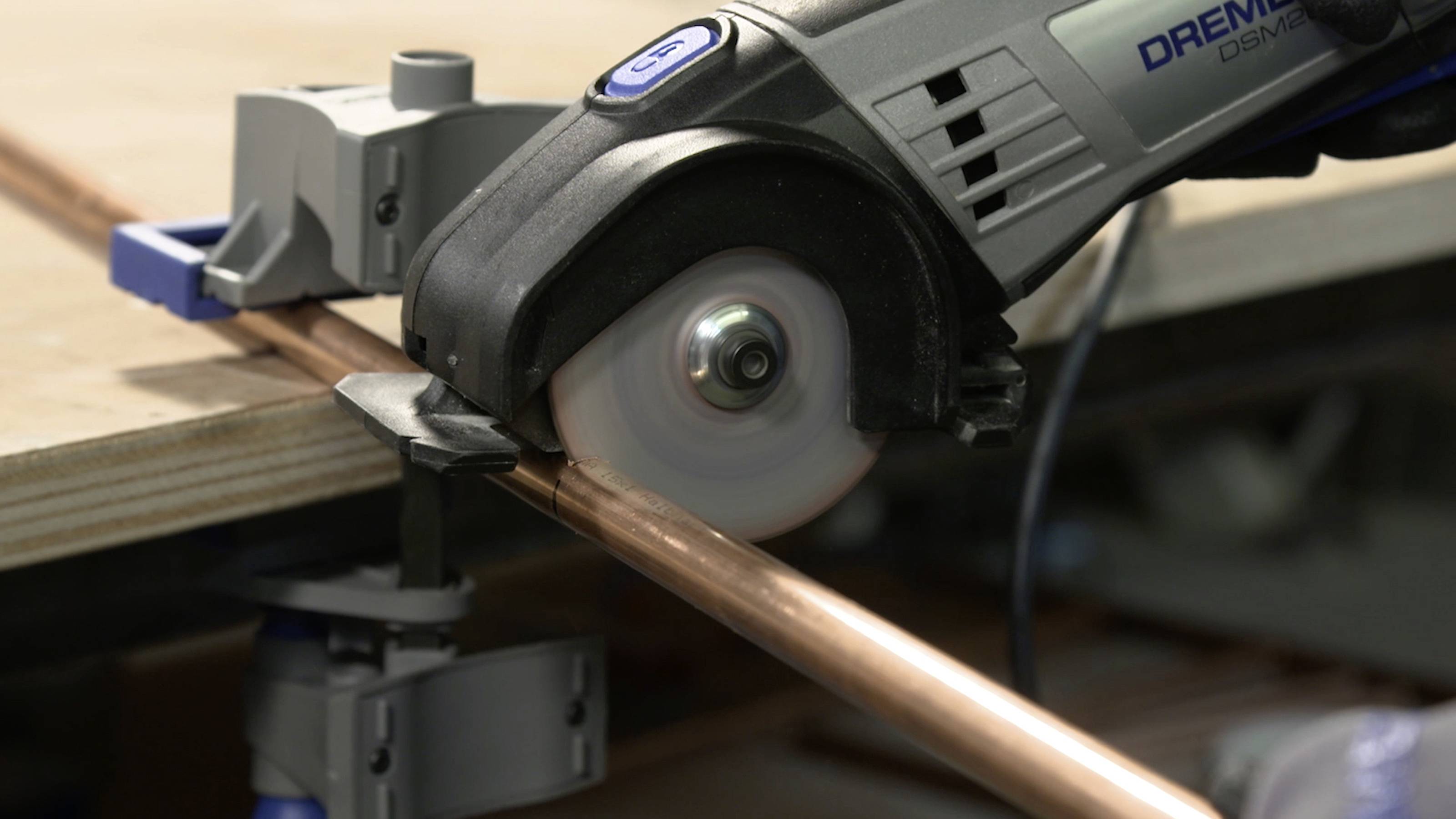 Eine elektrische Säge durchschneidet ein Kupferrohr, das an einem Tisch befestigt ist.