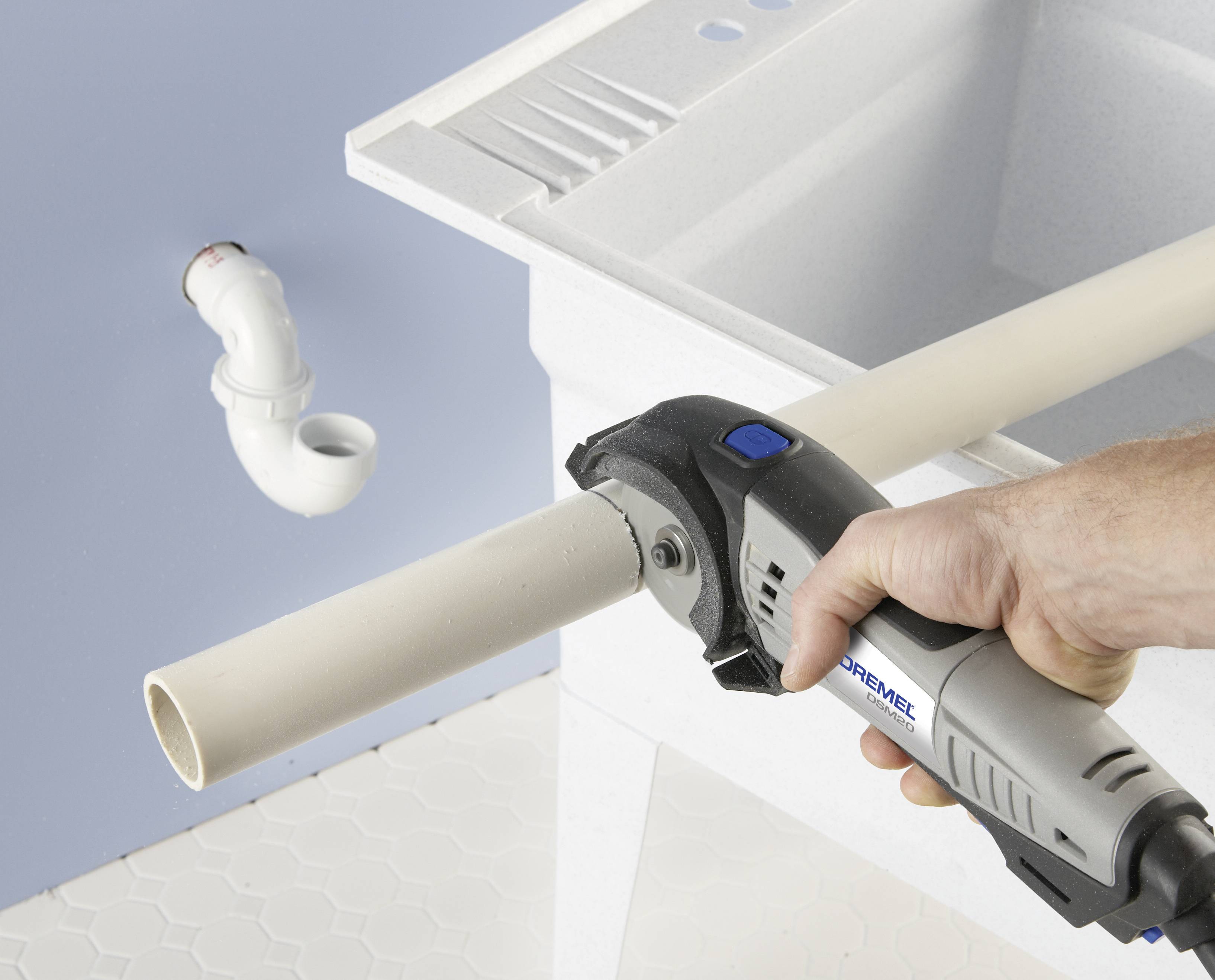 Eine Person schneidet ein PVC-Rohr mit einem Handwerkzeug neben einem Waschbecken; ein gebogenes Rohrstück ist im Hintergrund sichtbar.