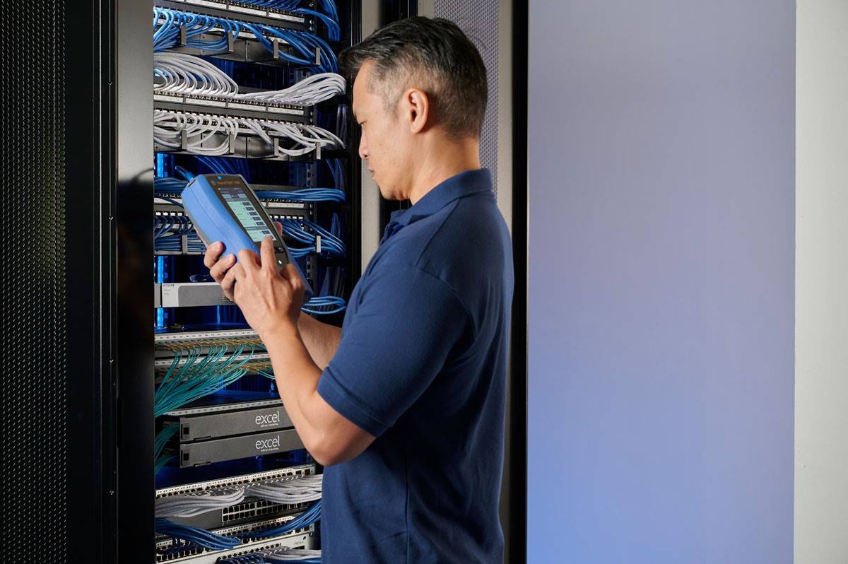 Ein Techniker in einem Serverraum überprüft mit einem Tablet die Konnektivität der Netzwerkkabel in einem Rack.