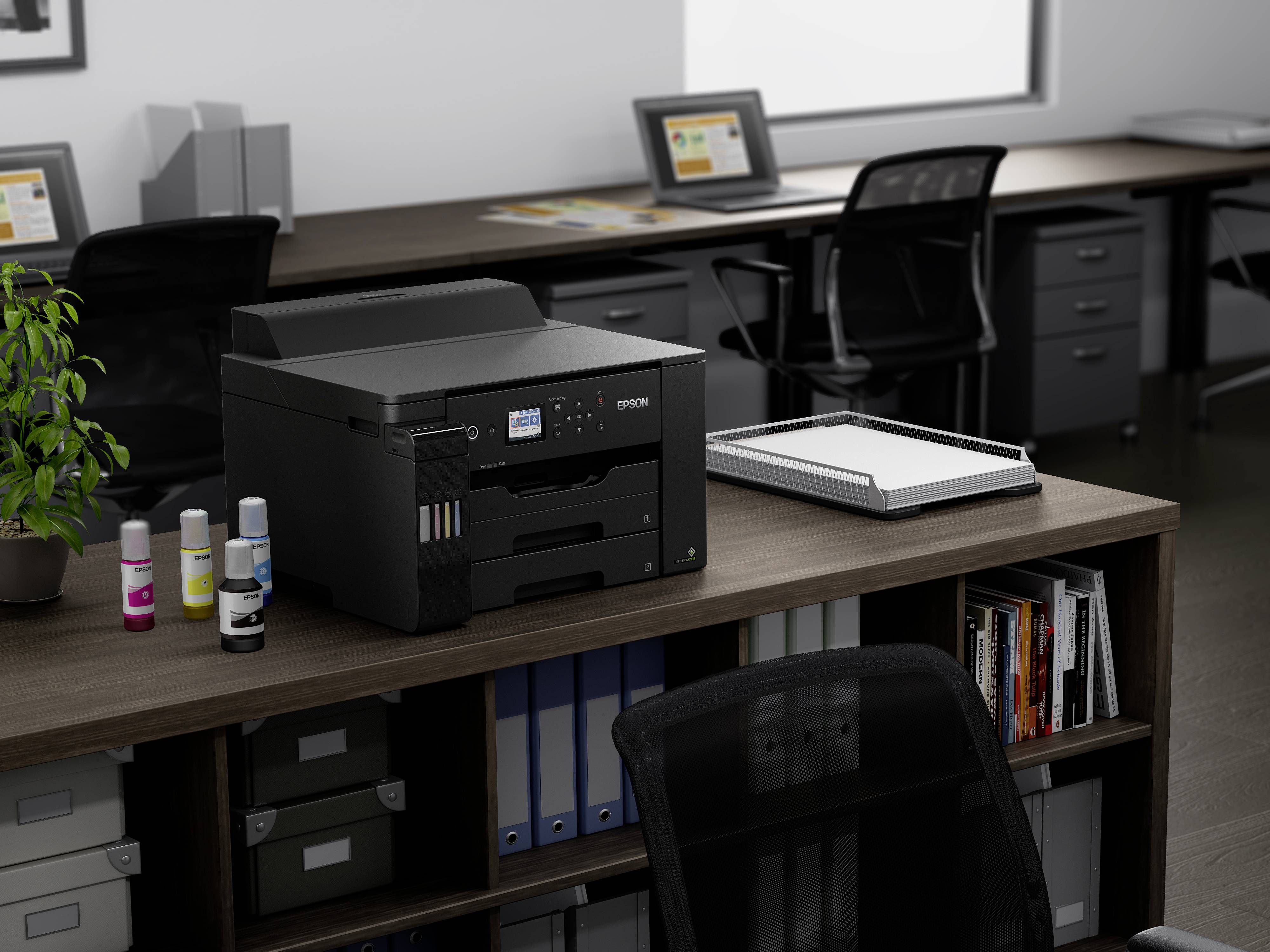 Drucker auf einem Büroschreibtisch mit Bürostühlen, Regalen und Büropflanzen im Hintergrund, bereit für den Einsatz im Arbeitsbereich.