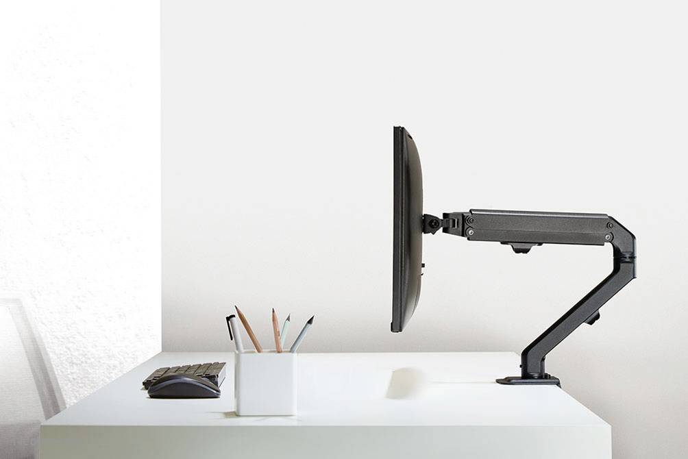 Ein Monitorarm hält einen Bildschirm seitlich über einem weißen Schreibtisch, daneben steht ein Stiftehalter mit farbigen Stiften.