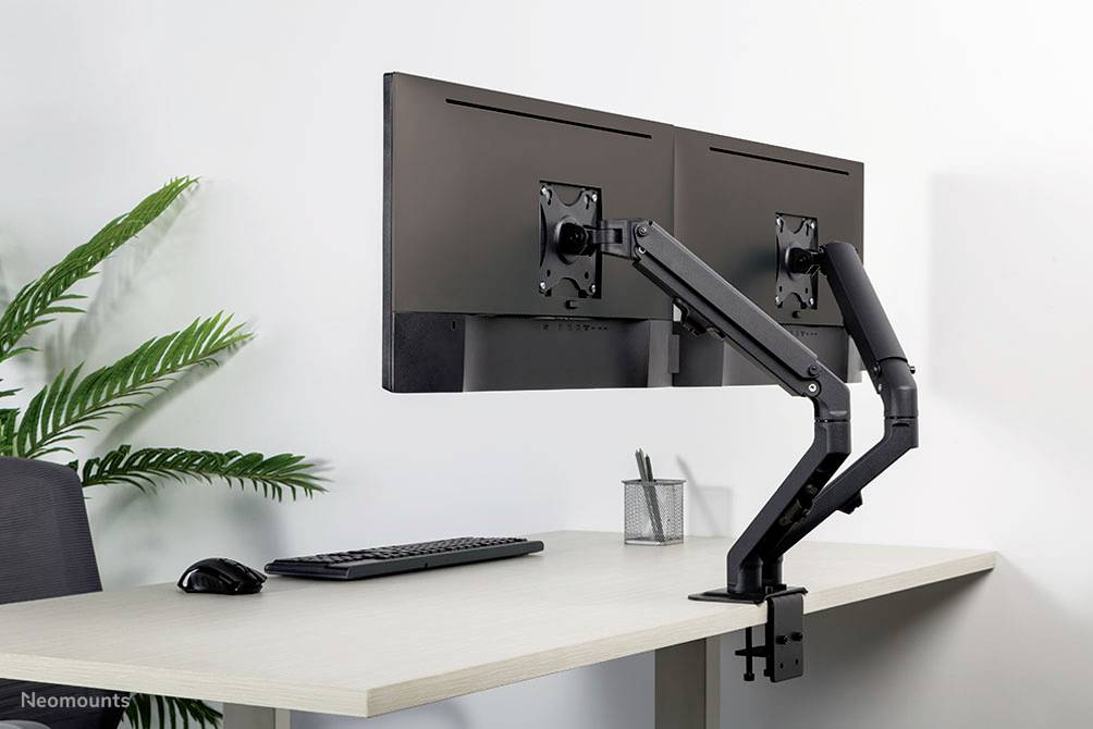 Doppelter Monitorhalter, befestigt an einem Schreibtisch, hält zwei Bildschirme horizontal nebeneinander. Auf dem Tisch sind Tastatur, Maus und Pflanze sichtbar.